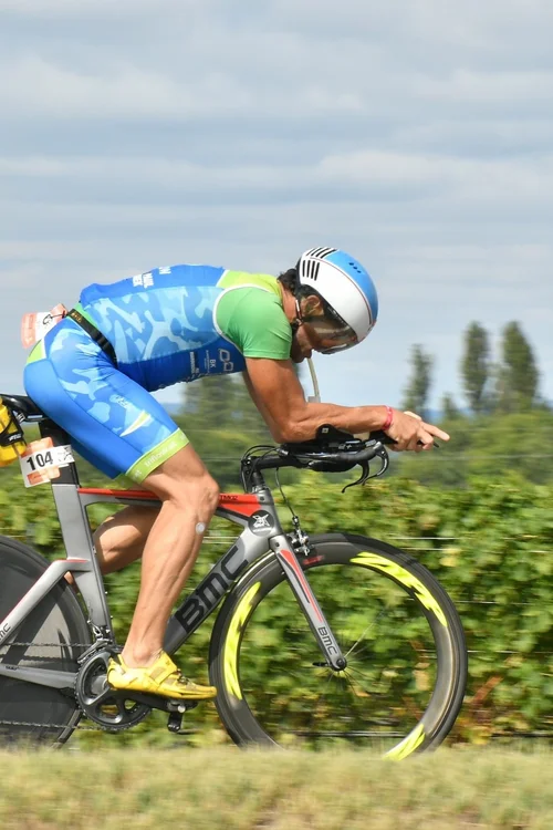 „Triathlet in Aero‑Position fährt ein Zeitfahrrad mit grünen Hecken im Hintergrund“